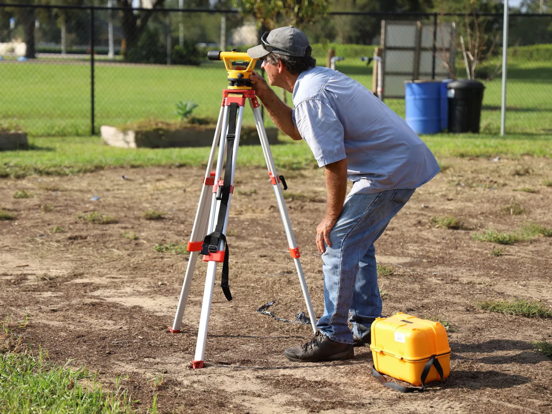 A surveyor sighting through a level mounted on a tripod in an open field.